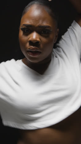 Vertical-Video-Full-Length-Studio-Shot-Of-Young-Woman-Wearing-Hoodie-Dancing-In-Spotlight-With-Shadow